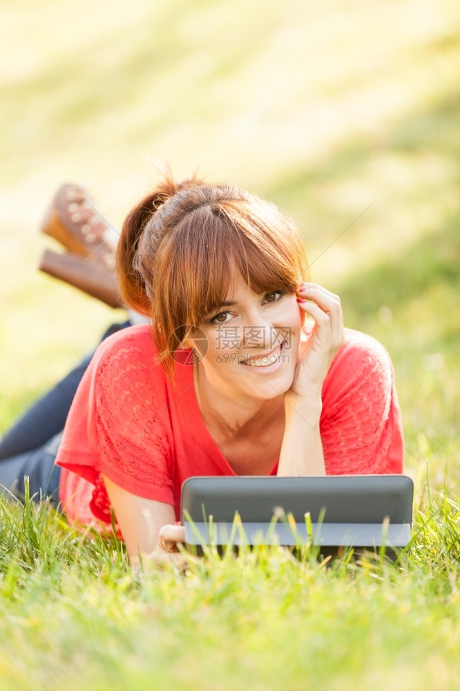 肖像互联网快乐的漂亮黑发美女躺在草地上看着数字平板电脑时躺在草地上图片