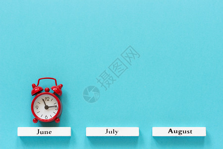 好的木制日历夏季月份和6在蓝色背景上的红闹钟概念月时间季节铺设背景图片