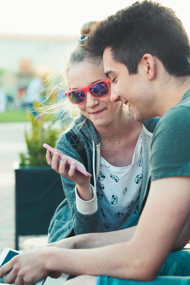 享受对话上市几个朋友十岁的女孩和男玩得开心用智能手机坐在市中心一起度过时间图片