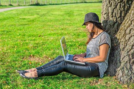 学习草地漂亮的在自然树上大腿操作计算机的年轻印度妇女图片