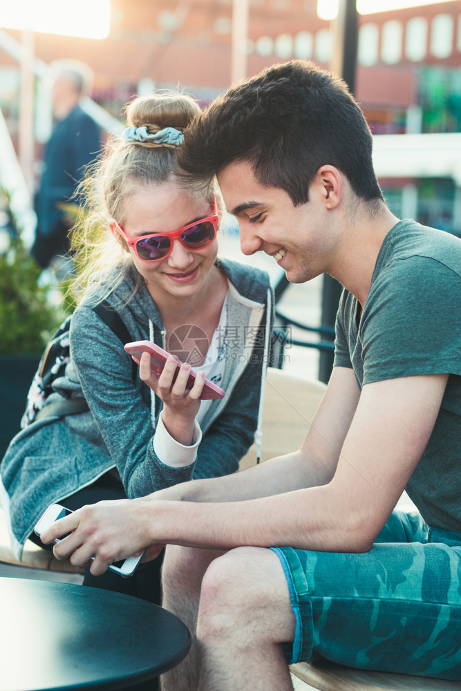 坦率几个朋友十岁的女孩和男玩得开心用智能手机坐在市中心一起度过时间开支发短信图片