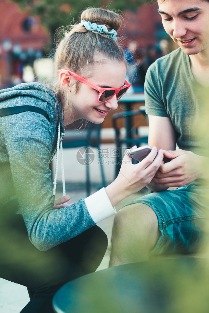男生发短信几个朋友十岁的女孩和男玩得开心的智能手机坐在镇中心一起度过时间坦率图片