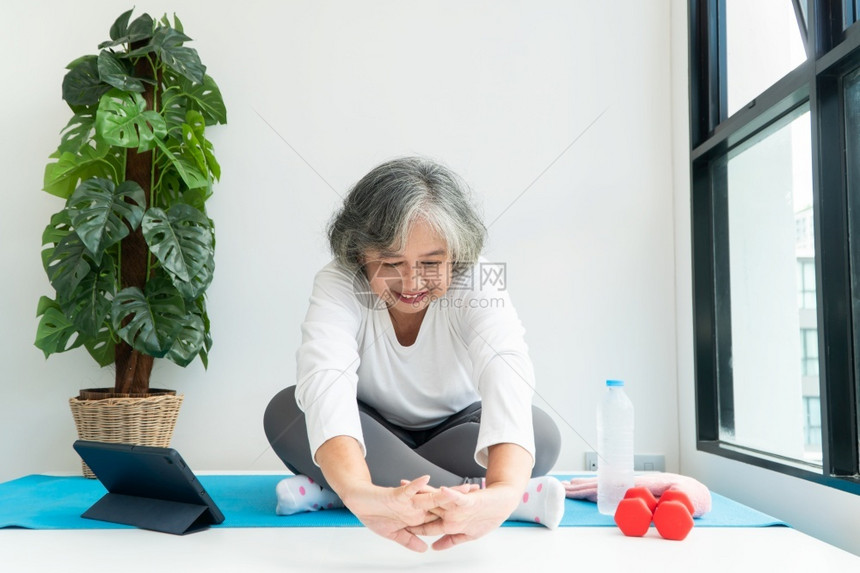 上笔记本电脑在线课程的亚洲老年妇女在家中起居室练习时观看膝上型计算机在线课程网上锻炼培训概念平衡班康复图片