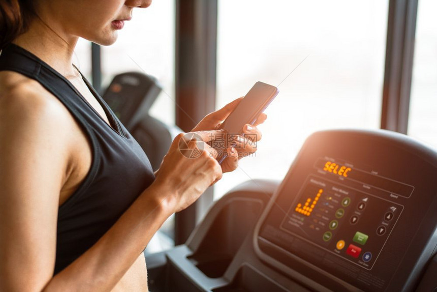 健身房运动或体力训练时使用智能电话的妇女在运动机放松和技术概念体育锻炼和保健主题快乐的人与舒适应用上进行运动或体力训练年轻的请享图片