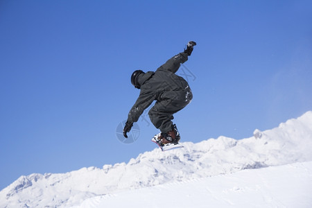 单板滑雪在阳光明媚的日子里高山上跳着极速跃的滑雪运动员空气阿尔卑斯山图片