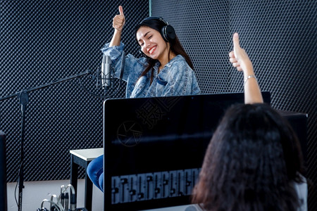 ps耳机素材制片人同事软件计算机监视器的女播音室技术员用于记录亚洲年轻女歌手在一专业演播室中唱着一首麦克风前方歌声的耳机情况PS电子的背景