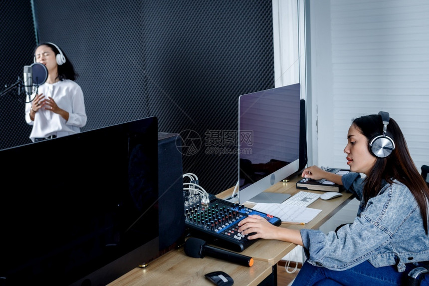 工作室专业的计算机监测器女技术员用于记录亚洲年轻女歌手控制台设备前的监控在专业演播室录制一首麦克风前的歌声录音带为年轻的亚洲女唱图片