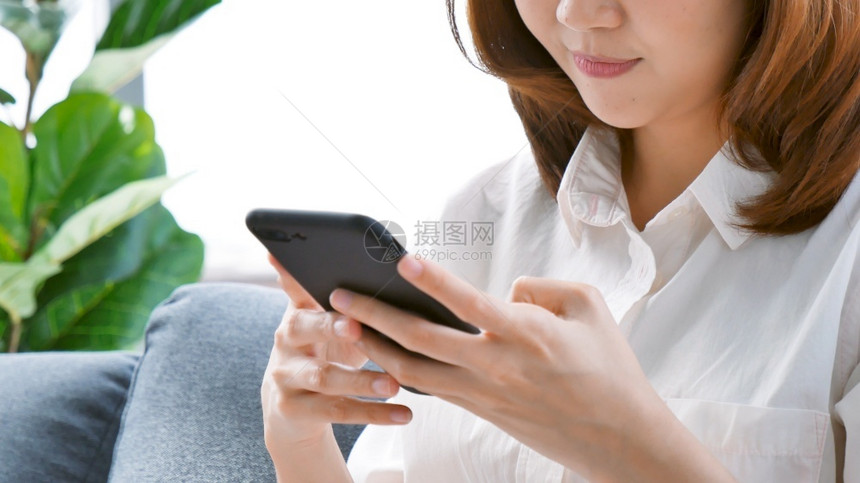 小工具抓住微笑面对亚洲女手持智能机与电子商务购物在线网站阅读文章博客视频年轻女手持电话技术生活方式女使用智能手机聪明的图片