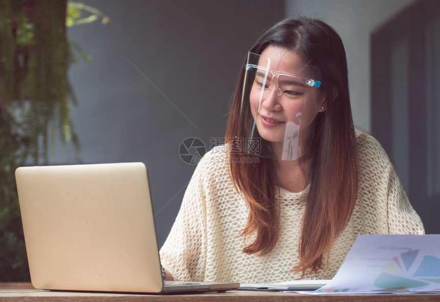 戴面具保护并使用移动电话和笔记本脑在家工作的新常识和技术概念亚洲美丽的妇女a利用手机和笔记本电脑在家中工作咖啡沟通互联网图片