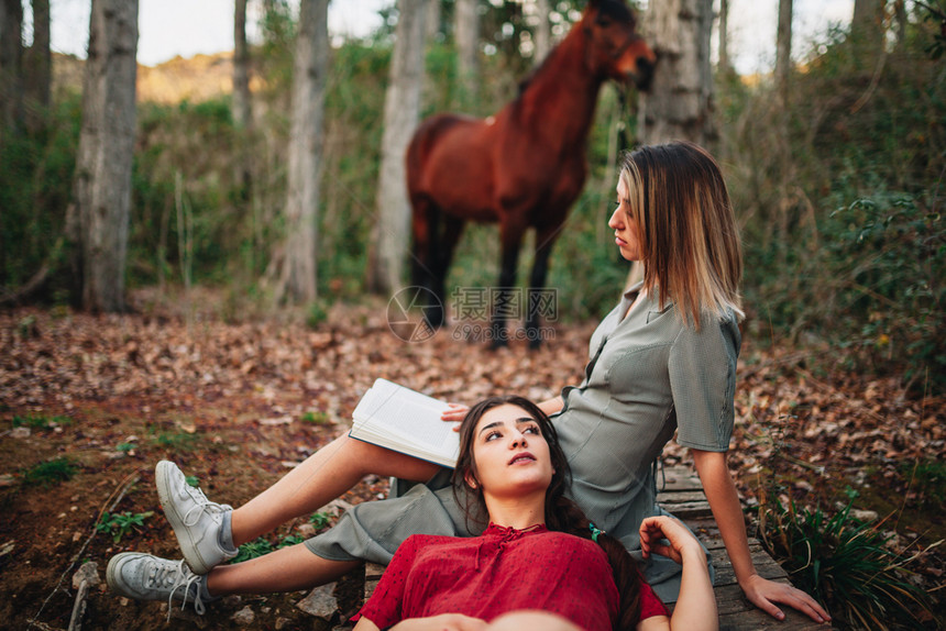 年轻一对身着洋装的年轻女子正在阅读一本书森林里用旧相机和马拍照旅行黑发派对图片