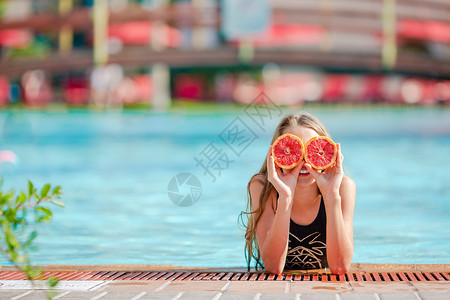 脸肖像美丽的小女孩用橘子遮眼睛在游泳池上被孤立的橙子遮眼睛在背景游泳池旁的眼里被柳橙子蒙睛背景图片
