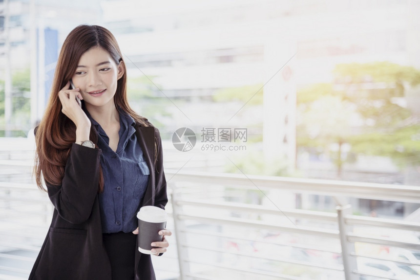 女士商人使用手机和微笑的面部电话进行商业交易职女工穿黑色西装手持智能电话谈论无线移动技术概念工作妇女穿黑色西装外部年轻的图片