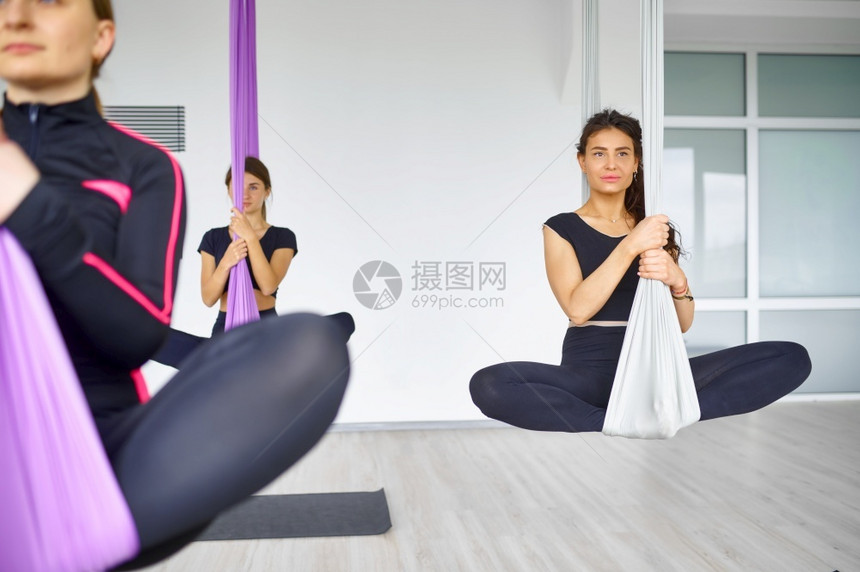 有氧俱乐部教练员空中瑜伽女团体培训挂吊床健身静肢和舞蹈锻炼混合了妇女参加运动室瑜伽的妇女悬吊床上的妇女团体空中瑜伽工作室运动的妇图片