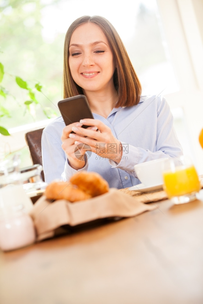 阅读商业照片为微笑的黑发女商人在检查她的电子邮件时吃早餐的照片橙图片
