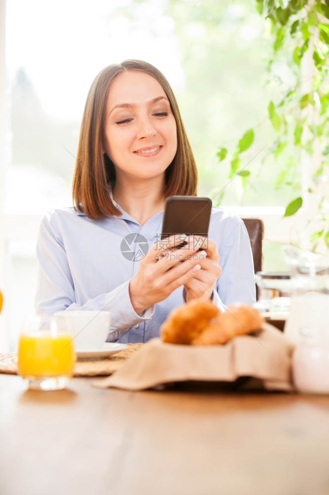 手机女士照片为微笑的黑发女商人在检查她的电子邮件时吃早餐的照片尽管图片