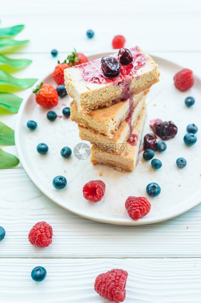 夏天经典芝士蛋糕的切片和白板奶酪蛋糕上的新鲜果子蓝莓和草关闭经典芝士蛋糕的切片和白色盘子上的新鲜果健康有机夏季甜点自制奶油的图片