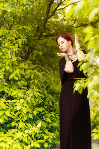 自然头发美丽的化妆品女孩身着黑色外衣和古董珠宝背景上绿色叶子感图片