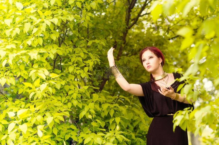 美丽的化妆品女孩身着黑色外衣和古董珠宝背景上绿色叶子脸树吸引人的图片