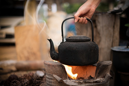 铁观茶抽烟野餐厨师紧握着煮水的手在火上装满旧茶壶背景模糊的木炭炉灶背景