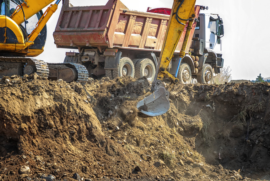 地点工业的舀挖土机正在卡车上装载挖掘作业重型建筑设备包括一个蓬顶或棍棒桶和旋转平台上的计程车等大型建筑设备图片