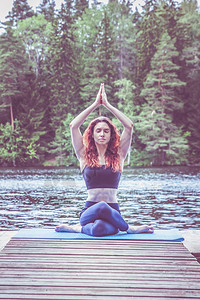码上有惊喜海报身体坐着放松年青瑜伽女孩在美丽的湖边码头上做瑜伽坐在不同的Gomukasana牛脸装扮中健康生活和自然平衡的概念背景