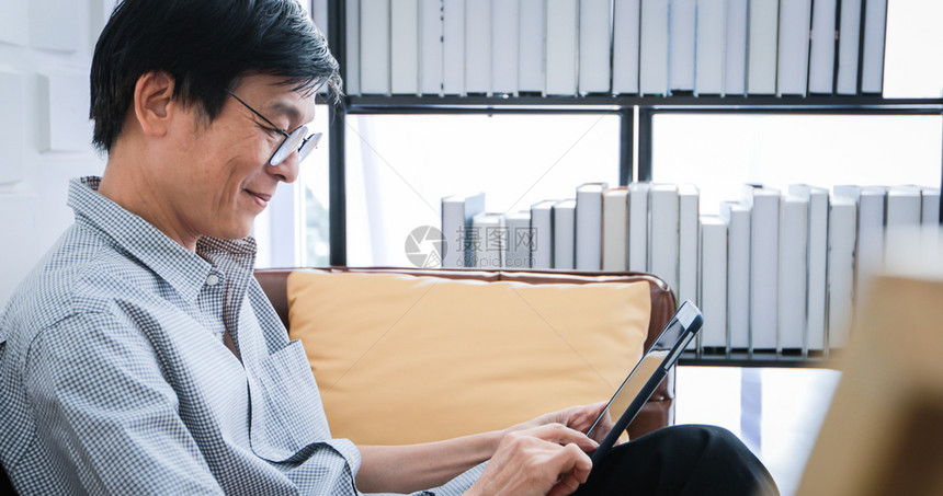 高级的亚裔老人在家中客厅沙发上玩平板和视频电话的亚洲老年人长者肖像正在放松与幸福并用平板游戏房间退休图片