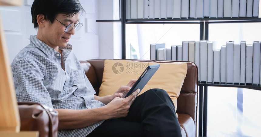 长椅成人互联网亚裔老在家中客厅沙发上玩平板和视频电话的亚洲老年人长者肖像正在放松与幸福并用平板游戏图片