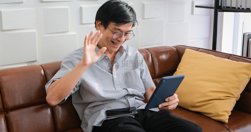 亚裔老人在家中客厅沙发上玩平板和视频电话的亚洲老年人长者肖像正在放松与幸福并用平板游戏长椅药片图片