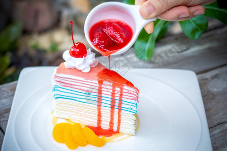 浇注彩虹crepe蛋糕和樱桃手倒草莓酱在顶上木质桌背景头绿色图片