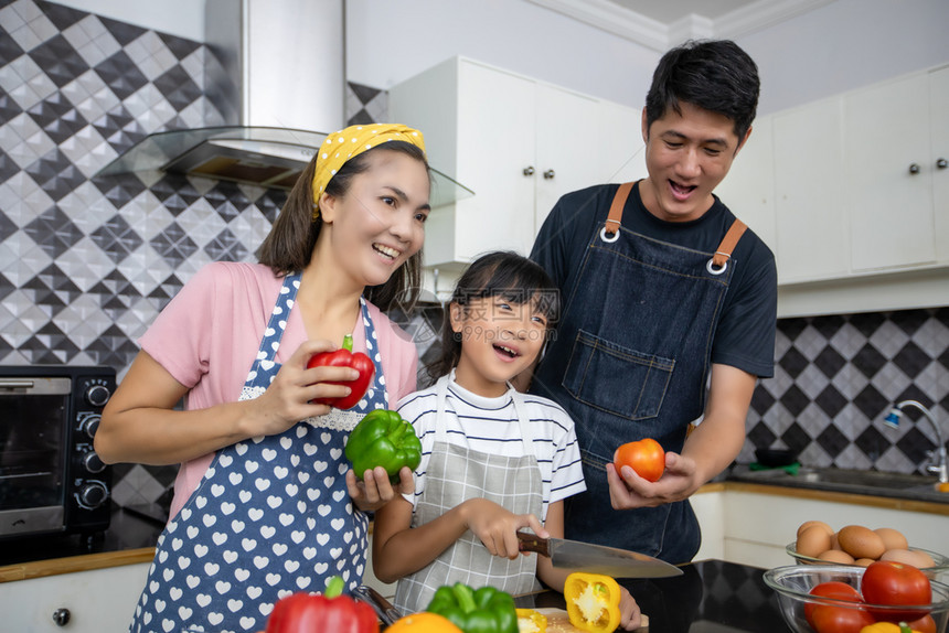 快乐的家庭有爸妈和她们的女儿在厨房一起烹饪笑声在室内父母女士图片