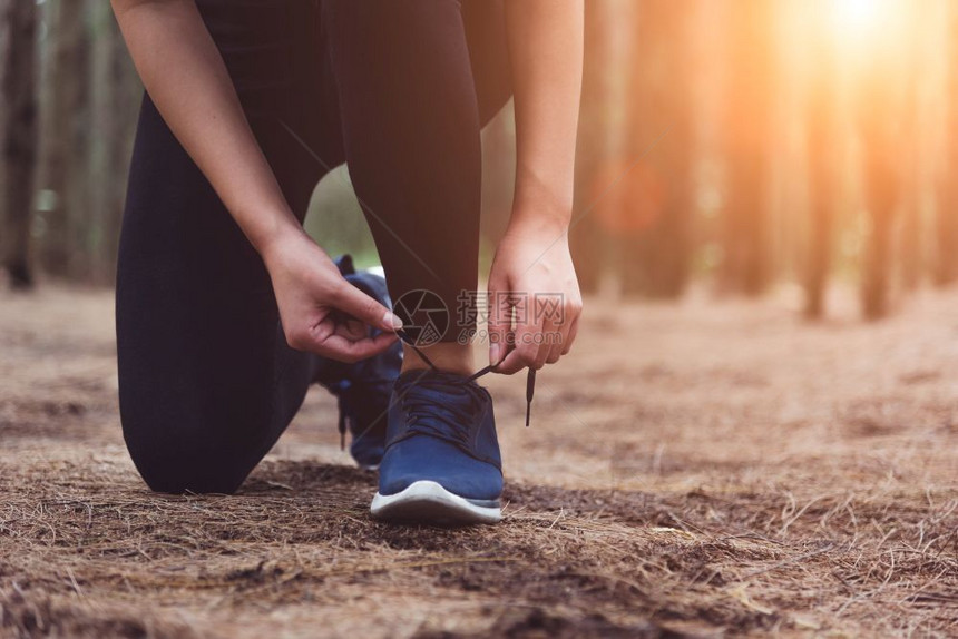 赛跑者女人在森林里慢跑时绑起鞋带着饮用水瓶回到森林边上妇女们用自来水瓶把人和生活方式概念捆绑在一起保健和福利主题公园和户外主题树图片