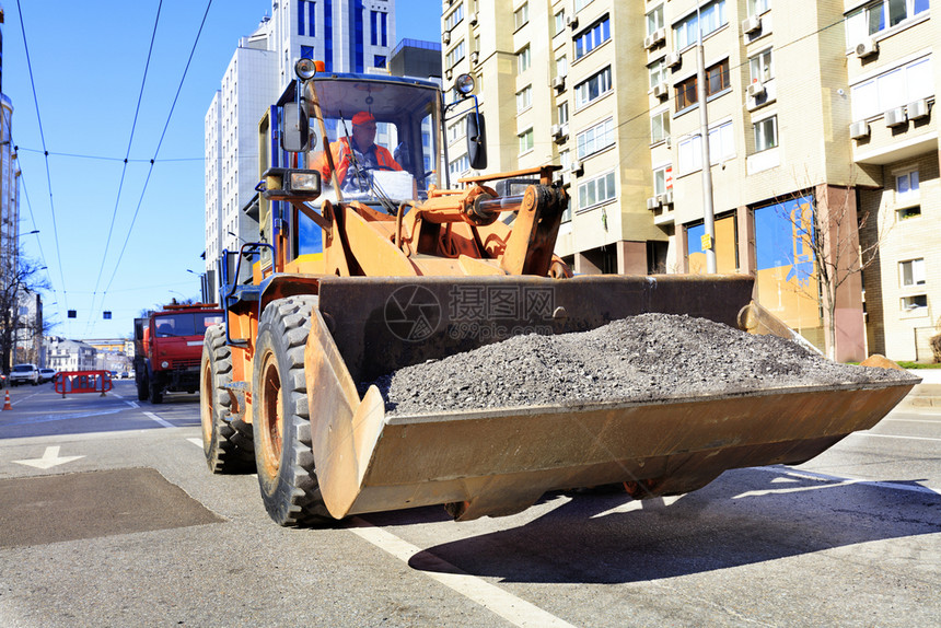 黑色的中午正对一个城市街道的公路建造过程中在一辆重型建筑推土机桶里用一台重型建筑推土机桶修理道路时一名工人将碎石塞在一辆重型建筑图片