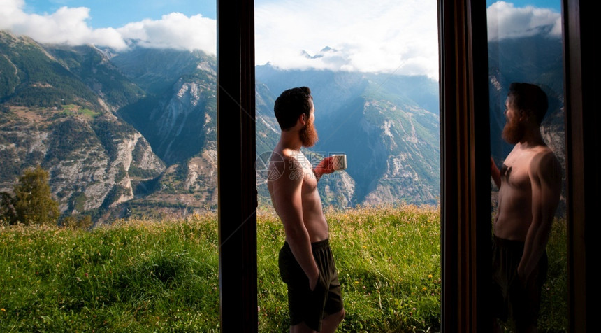 喝咖啡年轻人站在窗边欣赏美丽山景图片