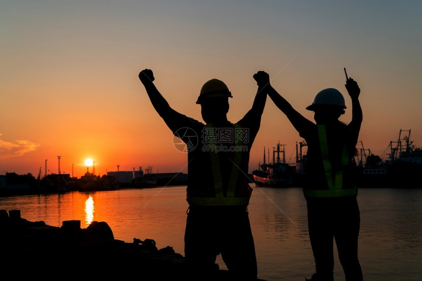 团队合作太阳提高手举起站在船厂的背景是石油储存的筒仓团队工作合以及成功概念在与工人和程师一起作时保持了团结精神图片