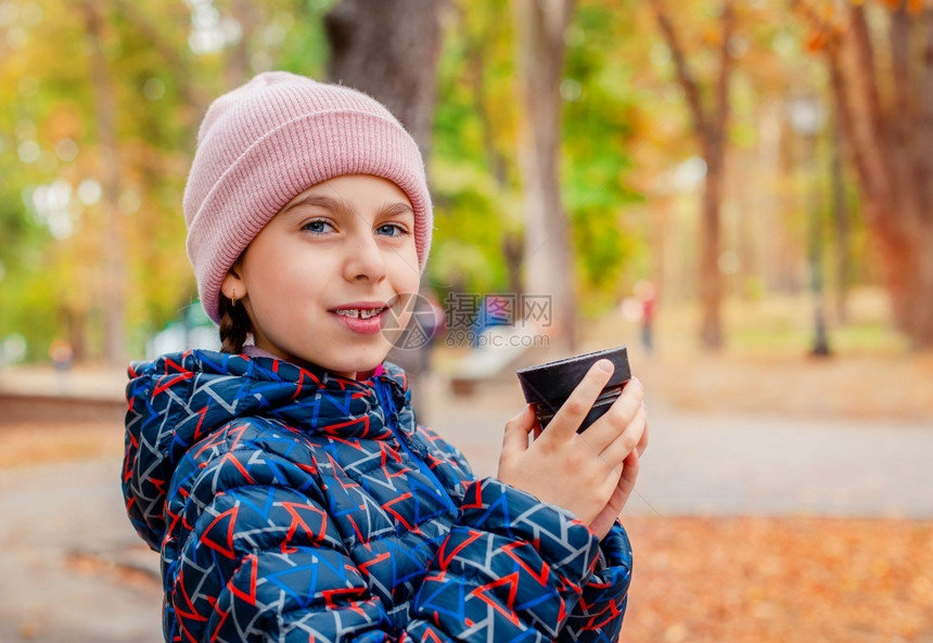 公园中快乐女孩在散步时喝着热茶休息秋天舒适的心情一个带着可爱微笑的孩子肖像在公园中快乐女孩与热茶一起散步秋日舒适的心情温暖脸户外图片