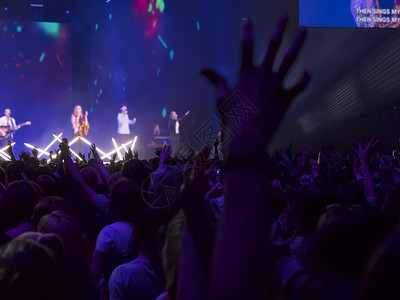 场地观众用双手在音乐节上举起手来灯光从舞台上下流而人群快乐的图片