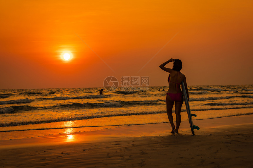 女孩模型旅游比基尼的年轻女在海滩上握手冲浪板和日落海景背下游暑假概念女客士图片