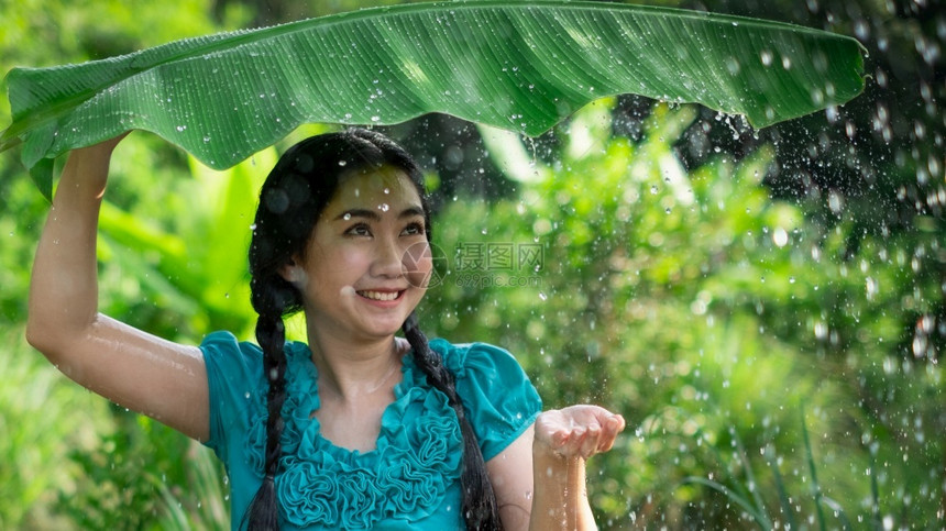分支乡村的一种在绿花园背景下雨时一位年轻亚洲女身着香蕉叶的黑头发肖像图片