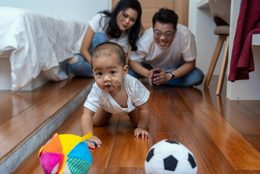 玩具亚洲男孩宝爬上木地板玩球照片模糊了父母在卧室里欢呼的模样家庭生活方式概念父亲和母在卧室中欢欣鼓舞愉快乐趣图片