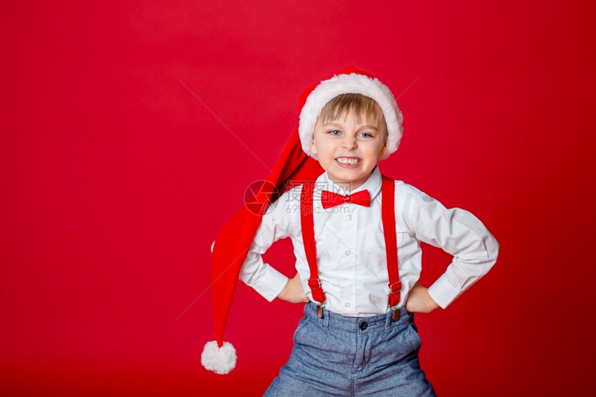 喜庆的圣诞快乐可爱开朗狡猾的小男孩戴着红色背景的圣诞老人帽子一个快乐的童年有梦想和礼物出去肖像图片