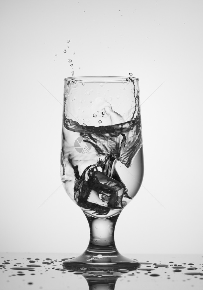 一种冰的立方体落入一个清晰的玻璃杯中墙壁和桌子上喷洒着一小滴水冰的立方体落入一个带水的玻璃杯中复制空间覆盖图片