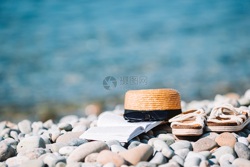 海滩概念草帽书太阳眼镜和在海滩上翻滚的沙帽子开着书上面有防晒霜和鞋假期优质的闲暇图片