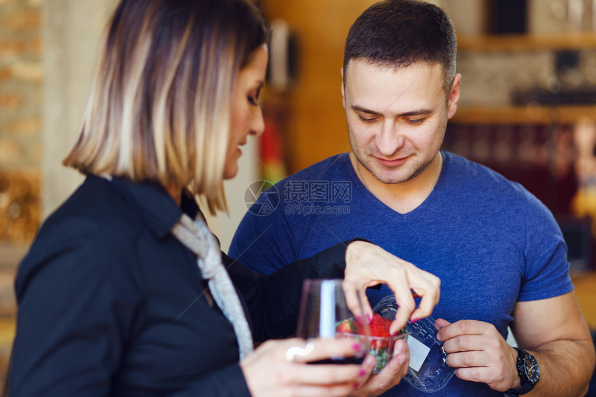 在家庭聚会日年轻成的天主教男女青年拿着一杯酒提供草莓穿着蓝衬衫快乐的侧观食物喝浪漫的图片