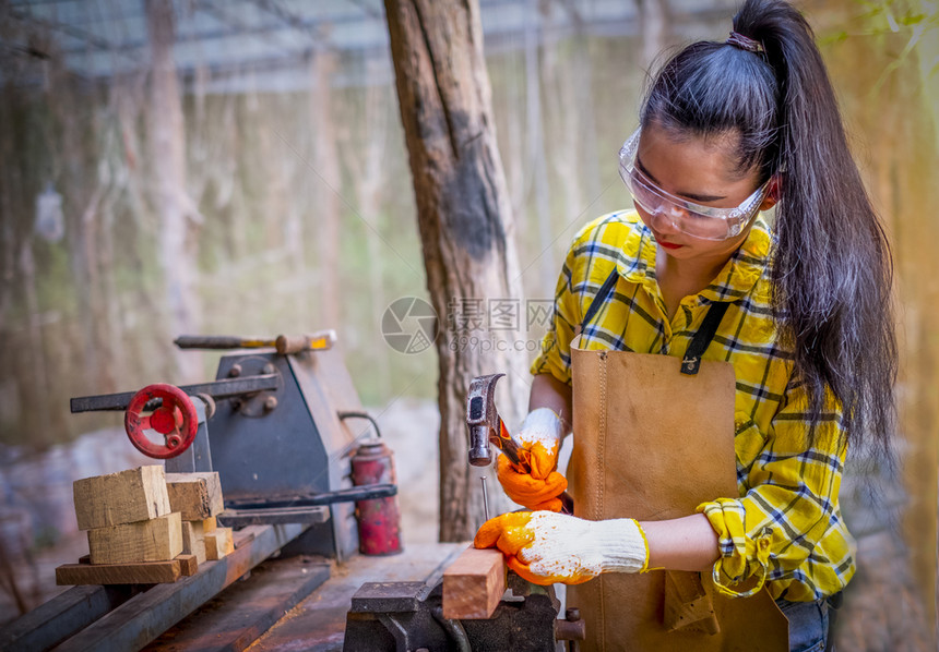妇女站立建筑工身着经检查的衬衫在建筑工地作在木板上钉弯曲内部的长椅图片