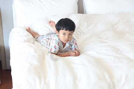 随便穿衣的亚裔男孩在床上穿衣服看照相机肖像特近身玩就寝时间愉快图片