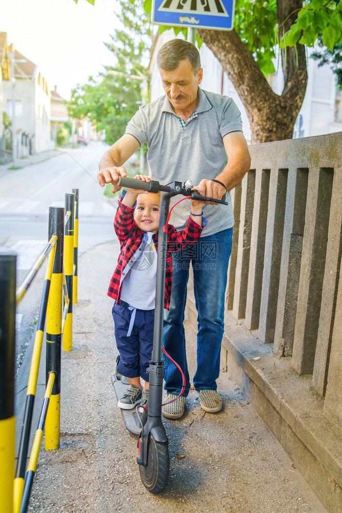 电的小男孩子在推踢脚踏车上与祖父的高级男子一起帮助他学会骑着人行道走移动男生图片