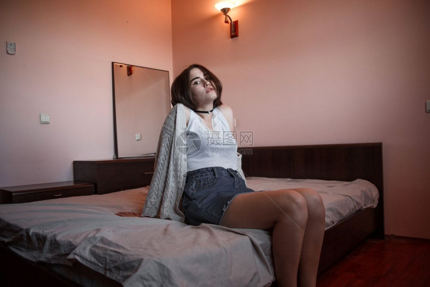 一个穿着毛衣短发和牛仔裙的年轻女孩独自坐在卧房的床上压抑中独居担心疲劳失望图片