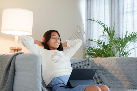 情感快乐的亚洲女孩在晚上坐客厅沙发时使用平板数码工具互联网尽管图片
