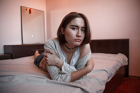 穿着毛衣短发的年轻女孩戴尼姆裙子单独躺在卧室的床上独自焦虑严肃图片