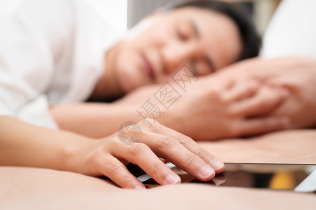 人们年轻妇女在床上睡觉时手握智能机以及放松聪明的图片